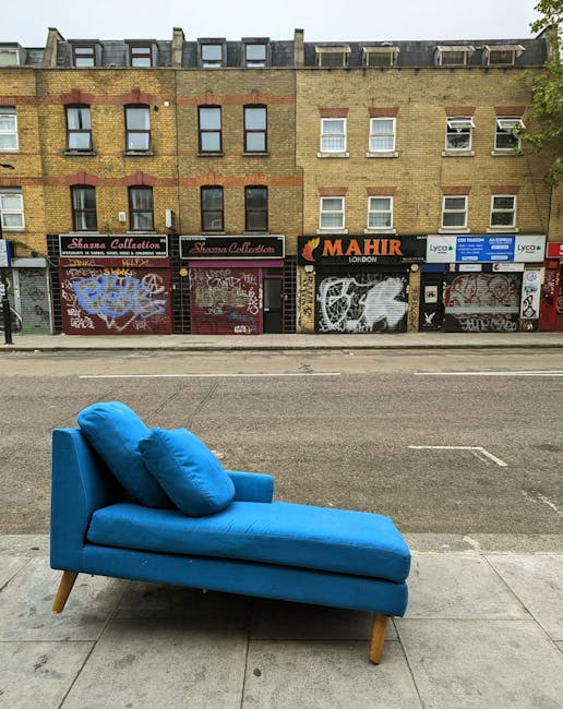 A vibrant blue chaise lounge with matching cushions is positioned on a concrete pavement outside a commercial building. The chaise features a wooden leg design and appears clean and well-maintained. B